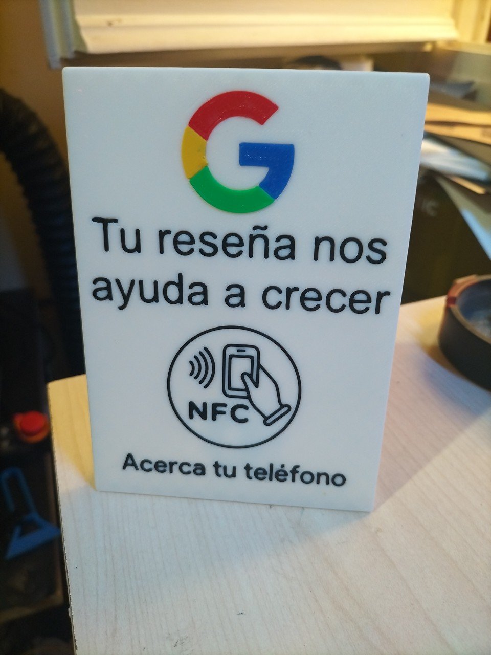 Placa NFC impresa en 3D con el texto Tu reseña nos ayuda a crecer sobre un mostrador
